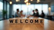 © Pete - Wooden cubes spell WELCOME on a table in a meeting room. Blurred background shows business people at a conference. Modern office environment, team collaboration, new beginnings.