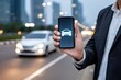 © Netsai - A person holds a smartphone showing a car icon, with a blurred city street and car in the background, suggesting ride-hailing or transportation services.