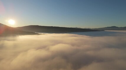 Wall Mural - Aerial drone footage of sunrise above mountains covered with a thick sea of clouds. Golden sunlight creates a dramatic and peaceful atmosphere, symbolizing nature, hope and inspiration.