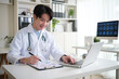 © wattana - Male doctor reviews patient data while working with a laptop and chart.