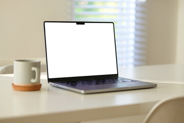 Wall Mural - Modern laptop with blank white screen and coffee cup on a minimalist white desk.
