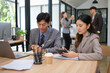 © wattana - Two young professionals reviewing business documents in a modern workspace.