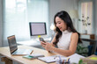© Wasana - Asian businesswoman using smartphone and working with laptop in modern office