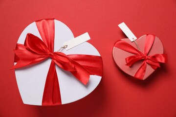 Wall Mural - Heart-shaped gift boxes with blank tags on red background, flat lay