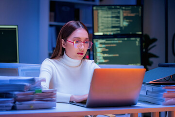 Asian programmer with glasses works late night shift in modern office, coding AI data analysis with artificial intelligence assistance for innovative tech solutions and machine learning development