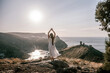 © svetograph - woman stands on a rocky hill overlooking a body of water. She is wearing a white dress and she is in a state of joy or celebration. Concept of freedom and happiness.