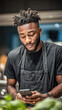 © Alla - Young african american man in black shirt and apron, focused on smartphone, surrounded by fresh ingredients, embodying the spirit of Friendsgiving celebration and culinary creativity