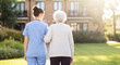 © Cla78 - Loving caregiver gently assists senior woman enjoying an afternoon stroll outdoors in a sunny assisted living community