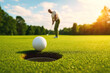 © Hq Visual Studio - Golf championship concept with close focus on ball near hole and player standing in background on professional course surrounded by trees and sunlight