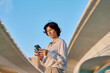 © we.bond.creations - Businesswoman using a mobile phone app while sitting under a highway overpass in the city, enjoying the convenience of technology