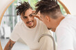 © Pixel-Shot - Young man with dreadlocks looking in mirror at home