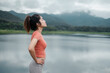 © Satori Studio - Woman in activewear stands by a tranquil lake, surrounded by mountains and clouds, enjoying the peaceful natural scenery.