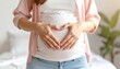 © Muzaki - Pregnant woman gently cradles growing baby bump, forming heart shape with hands, expressing love and anticipation.