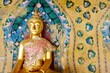 Gold Buddha statue clothed in traditional Thai silk garments with ancient painted backdrop at Wat Arun, the Temple of Dawn in Bangkok, Thailand
