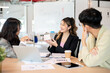 © bongkarn - Smiling asian businesswoman holding or showing calculator to coworker while having meeting in office