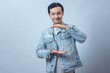 © Daniel - Asian man in denim jacket smiling and making space between hands as if holding invisible object against plain studio background, showing product presentation or measurement gesture in lifestyle pose
