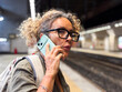 © simona - Middle-aged woman on phone in underground train station, worried and waiting for subway or train, showing concern, stress, anticipation and real life moments of urban commuting and everyday travel