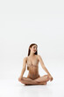 © Lustre Art Group  - Poster. Sitting cross-legged in nude lingerie, young woman looks peaceful, with soft smile, as she stretches against white studio background. Concept of wellness, natural beauty, spa procedures.
