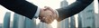 © JT Studio - Two businessmen shake hands against a city skyline, symbolizing partnership and collaboration in a professional setting.