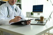 © saltdium - Close-up of a medical professional reviewing a patient chart and enters information into a laptop during a focused work session