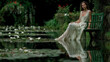 © LarisaM - A woman in a white dress sits on a bench in a pond. The water is calm and the surrounding area is lush with greenery. The scene is serene and peaceful, with the woman appearing to be lost in thought