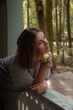© Sofia - Woman with short brown hair holds a green apple near her face while leaning on a rustic wooden railing in a forest park in Peredelkino