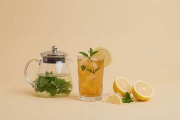Wall Mural - Glass of iced lemon tea with mint and a teapot on a light beige surface