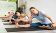 © JackF - Young woman maintaining mental and physical health attending group yoga class at studio, practicing stretching poses
