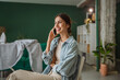 © Miljan Živković - Smiling woman talking on mobile phone while sitting on chair at home