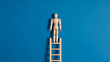 © Fiaz Gulab  - Wooden mannequin figure stands on a ladder against a vibrant blue background, symbolizing ambition and progress.
