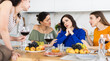 © JackF - Upset young brunette sitting at home table during cozy friendly gathering while attentive besties comforting and supporting her, discussing problems and giving advice over glass of wine