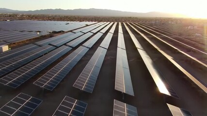 Expansive solar farm with long rows of photovoltaic panels in a desert landscape at sunset.