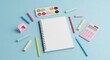 © Ilham - Blank notepad surrounded by art supplies chalk, watercolors, calculator, pencils on a blue background. Back to school flat lay style composition.