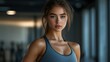 © ProPhotos - In a modern gym setting, a young athletic woman glances at the camera, her fitness gear accentuating her active lifestyle and commitment to health.