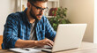 © Kaluya Stock - Focused young man in glasses typing intently on a laptop at a wooden desk, working from home or office