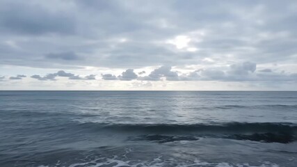 Wall Mural - Calm Ocean Waves Under Cloudy Sky - Serene view of gentle ocean waves rolling towards the shore under a cloudy sky. The tranquil scene evokes a sense of peace and calmness.