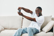 © SHOTPRIME STUDIO - Happy young African man enjoying video games on a couch, showcasing excitement in a casual home setting, perfect for gaming niche