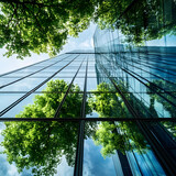 Modern glass skyscraper reflecting lush green trees and blue sky