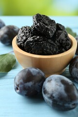 Wall Mural - Dried prunes in bowl, leaf and fresh plums on light blue wooden table, closeup