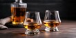 © Thanagorn - A close-up of two elegant whiskey glasses filled with amber liquid, set against a dark backdrop, creating a sophisticated and inviting atmosphere.