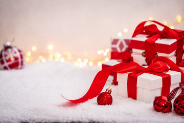 Wall Mural - festive white gift box tied with a red ribbon, resting on snow with blurred golden lights in the bac