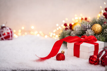 Wall Mural - white gift box with red ribbon and ornaments under snowy branches, set against warm holiday lights. 