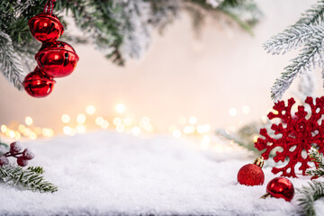 Wall Mural - festive red baubles rest on snow beneath frosted pine branches and golden holiday lights in the back