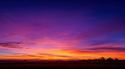 Wall Mural - Soft pastel hues of purple pink and orange fill the sky as the sun sets behind a peaceful countryside. The serene landscape invites calm reflection and admiration of natures beauty.