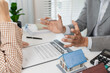 © PHOTO4U - A real estate agent and client are discussing property purchase options, reviewing a contract, calculating loan terms, and considering house models as part of a housing investment decision.