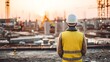 © Pickoloh - A construction worker in a safety vest and hard hat observing a construction site with scaffolding and building structures in the background