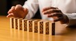 © iCreative - A man is about to push a domino in a row of dominoes on a wooden table