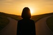 © なにがしあれこれ - 美しい夕日を前に、二つの道が分かれる岐路に立つ女性のシルエット。人生の選択、キャリアの決断、そして未来への希望と不確実性を象徴する、エモーショナルでコンセプチュアルなイメージ。