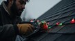 © Svitlana Vorotniak - Man attaching Christmas string lights to a roof shingle with a staple gun. Holiday decoration concept for home exterior. Preparation for Christmas.