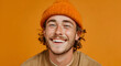 © Daniel - Happy gen Z young man with mustache wearing khaki blouse and orange beanie smiling at camera. Studio shot, beige background.